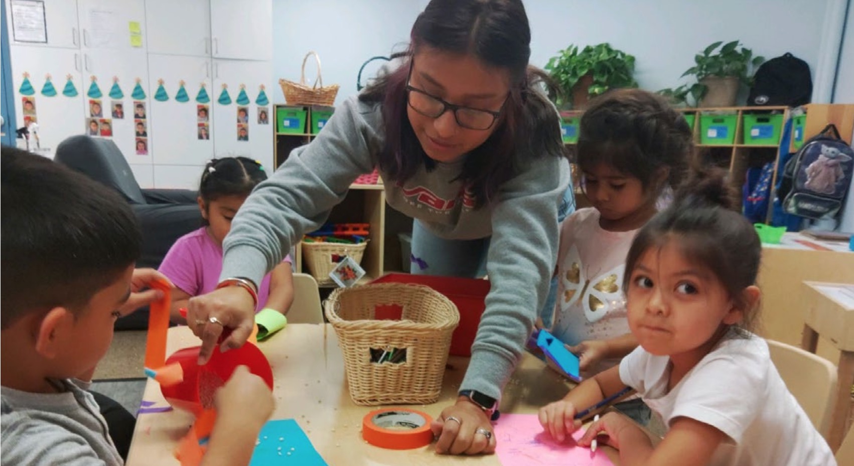 A teacher assisting several children with a craft project